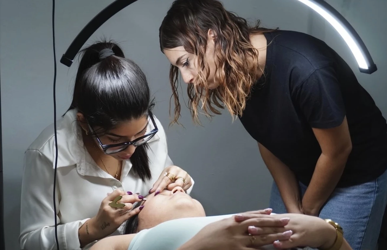 Ángela demuestra una técnica de cejas mientras una alumna observa